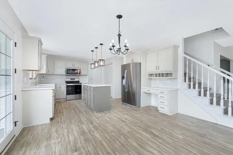 A Renovated Kitchen With White Cabinets, An Island And Pendant Lights