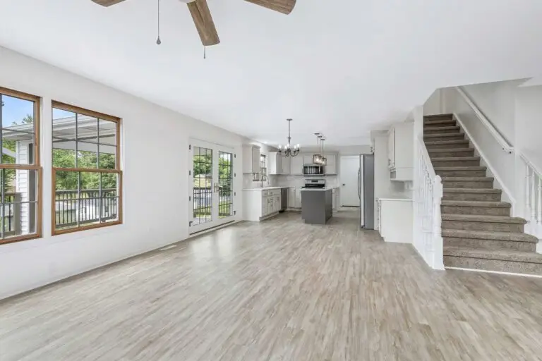 A Renovated Open Living And Dining Room With New Flooring, White Walls And A Staircase
